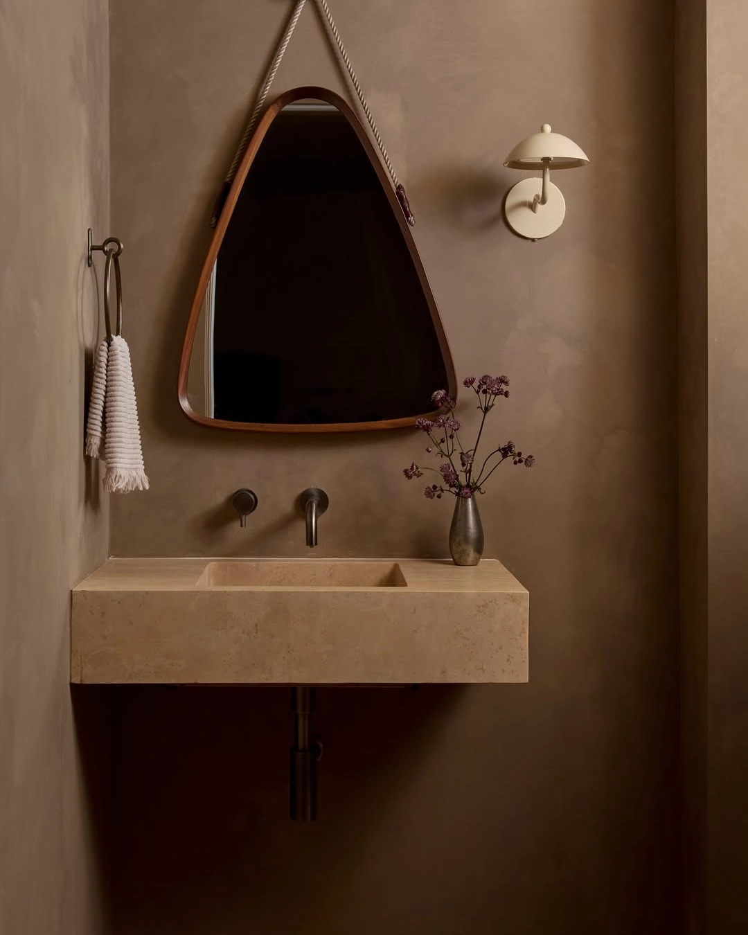 Beige limewash bathroom walls with a stone sink and dark mirror