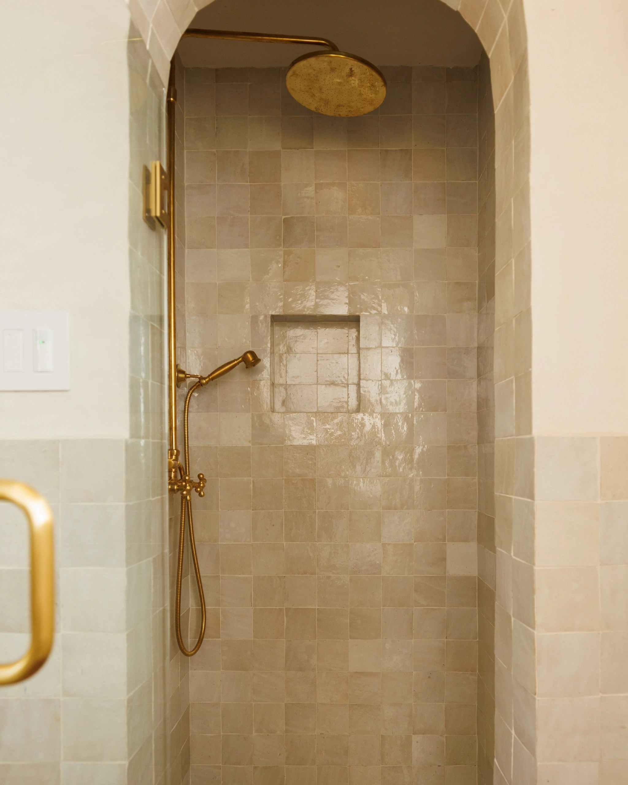 Beige zellige-style shower tiles with brass fixtures