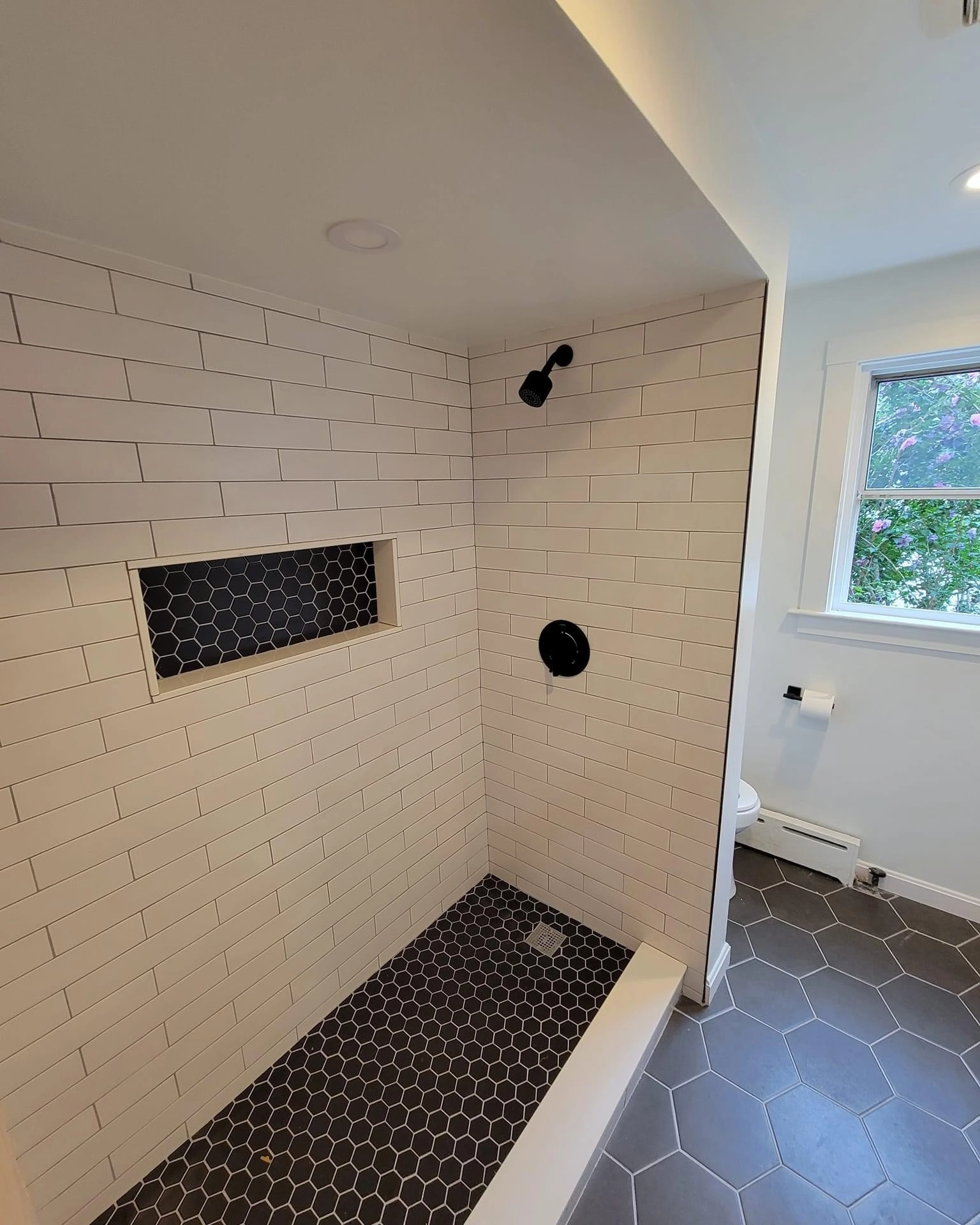 Black hexagon floor tiles inside a beige and white shower