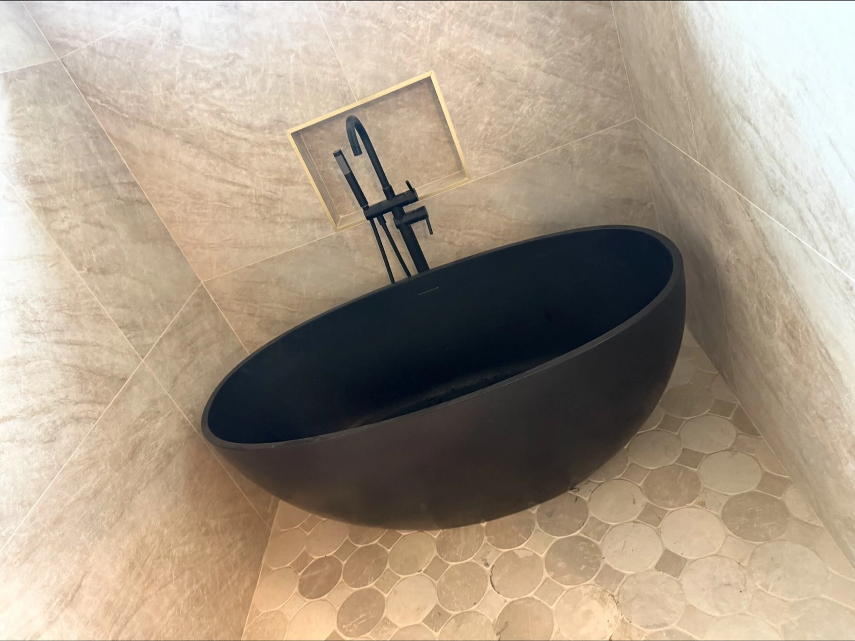 Black freestanding tub against beige marble-look tiles