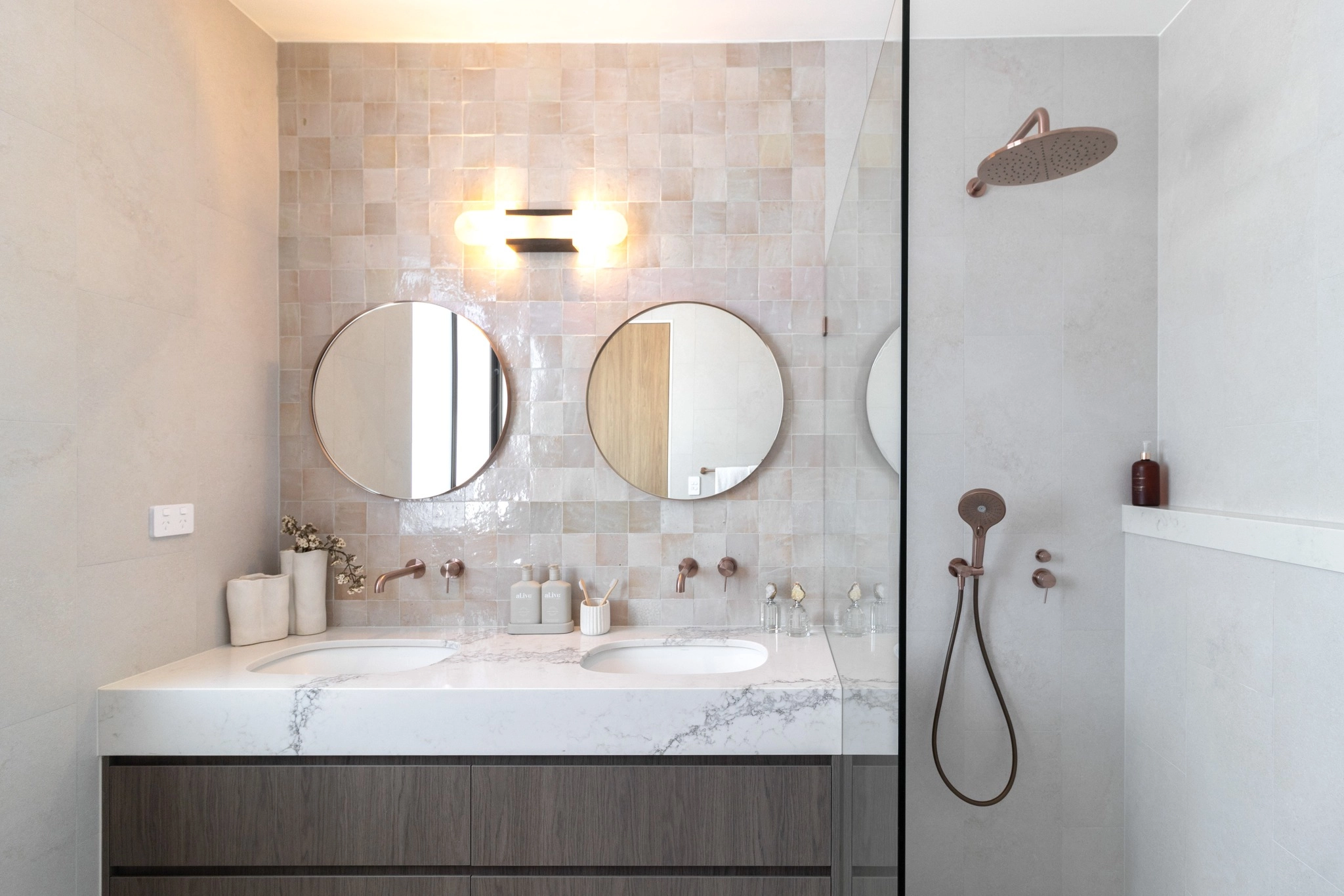 Thin-framed round mirrors over a beige tiled vanity wall
