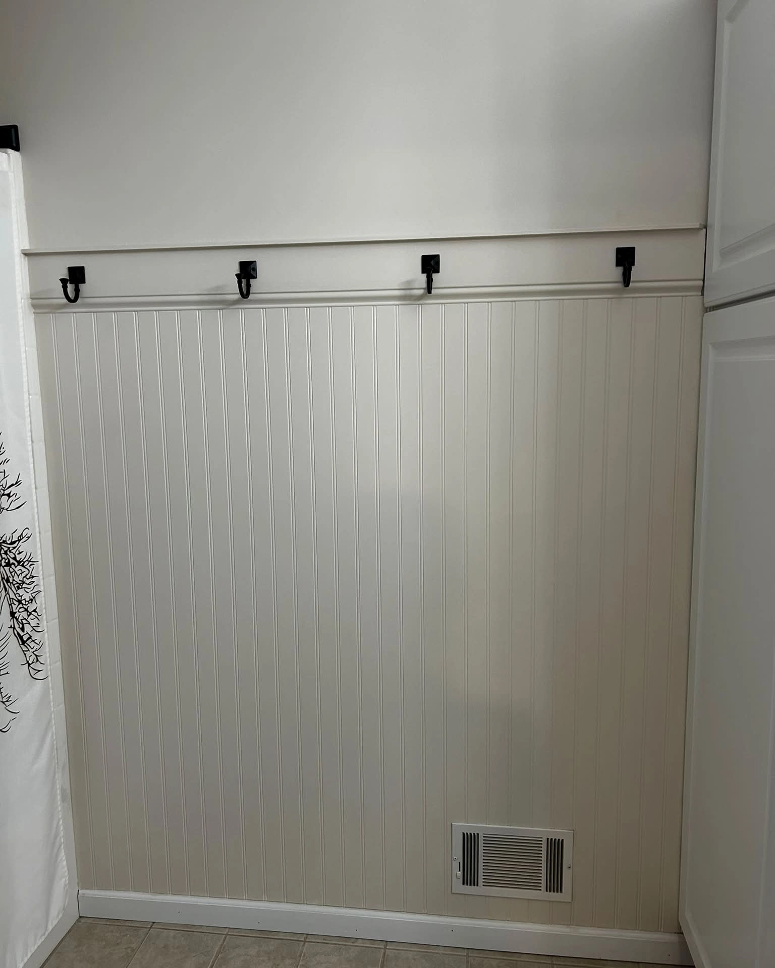 White beadboard half wall with black hooks in a bathroom